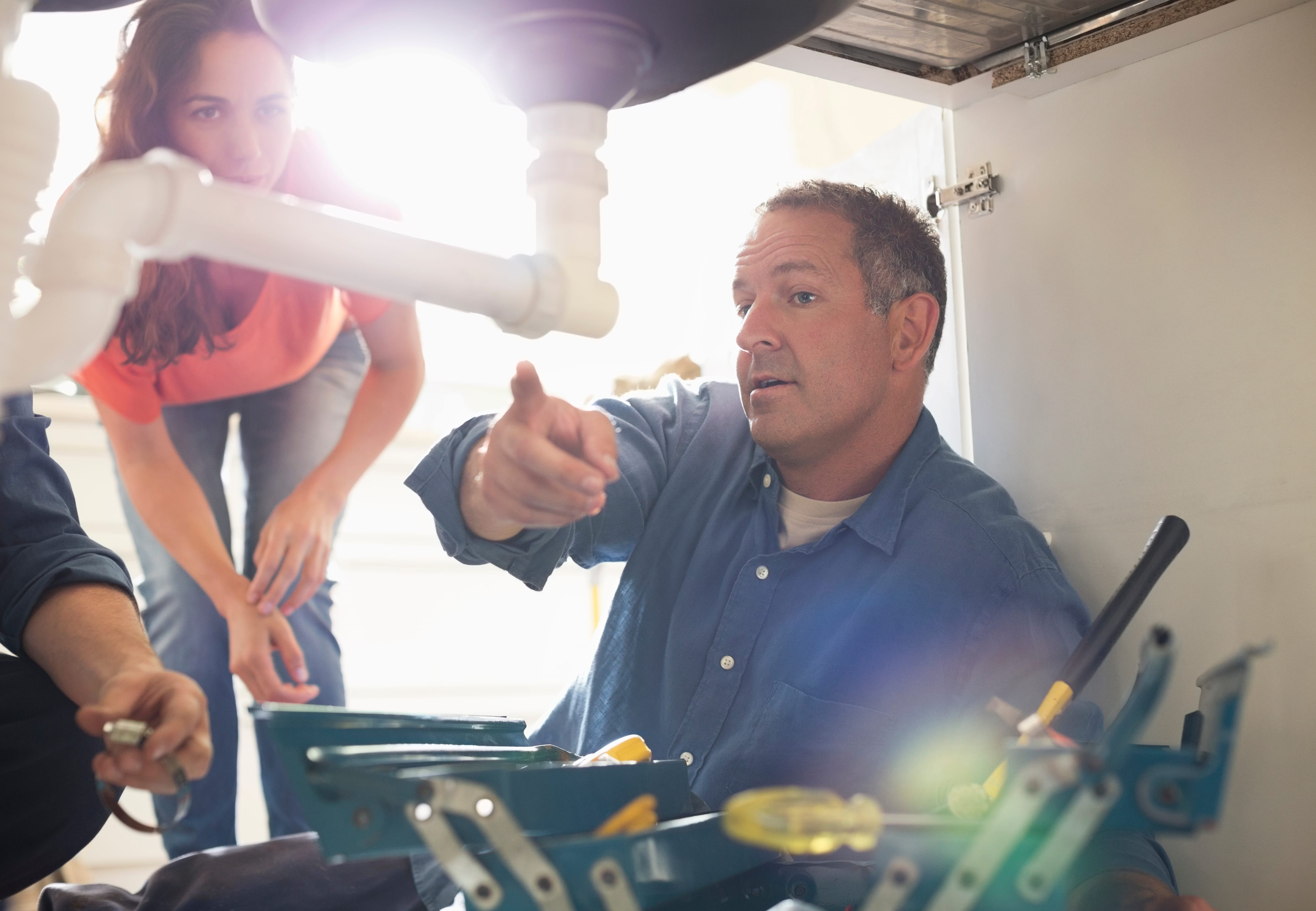 Plumber on a job fixing pipes underneath a sink for women with a commercial van hire for plumbers from hirefleet.