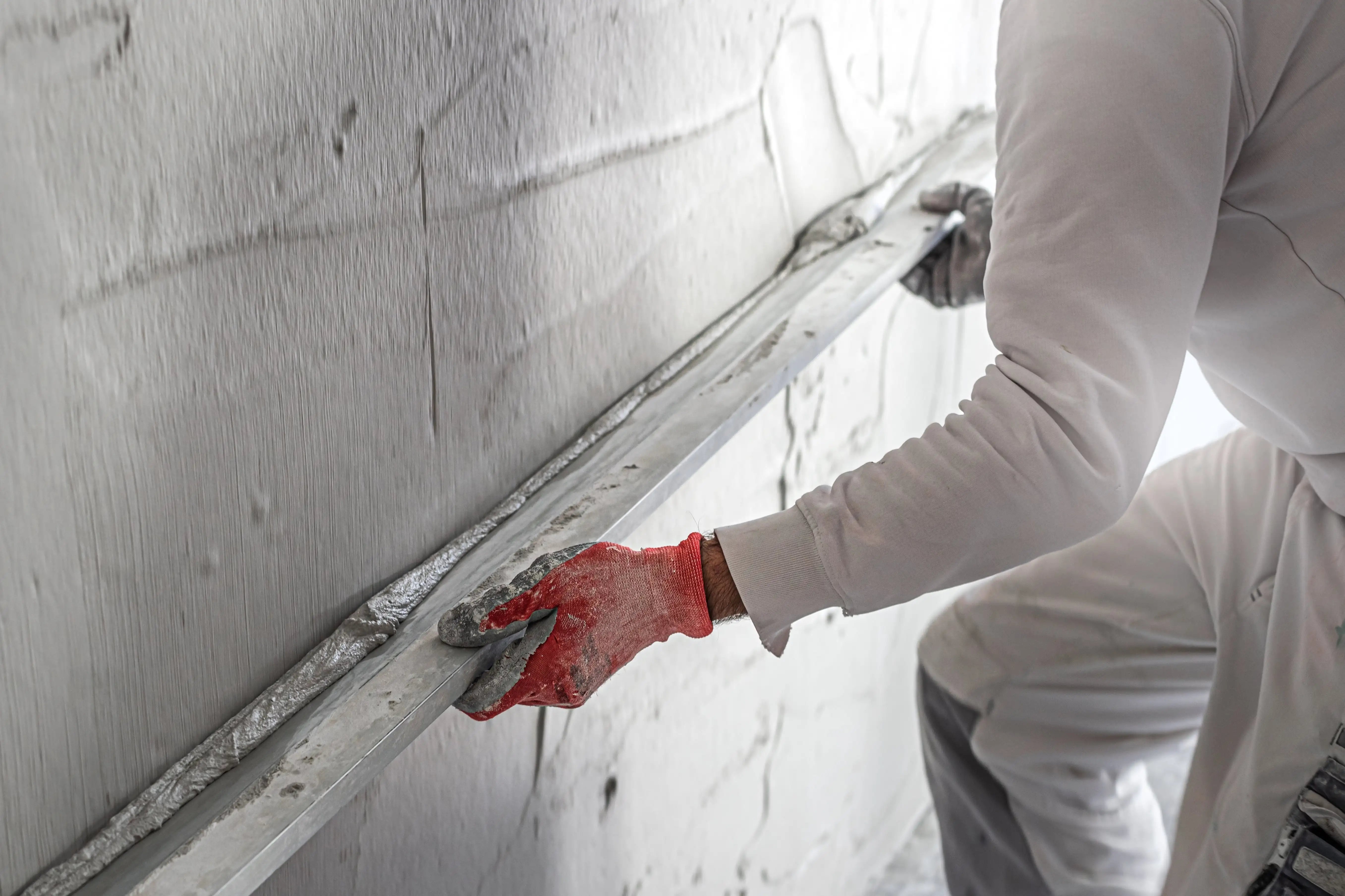 Man with red gloves plastering a wall with commercial van hire for plasterers.